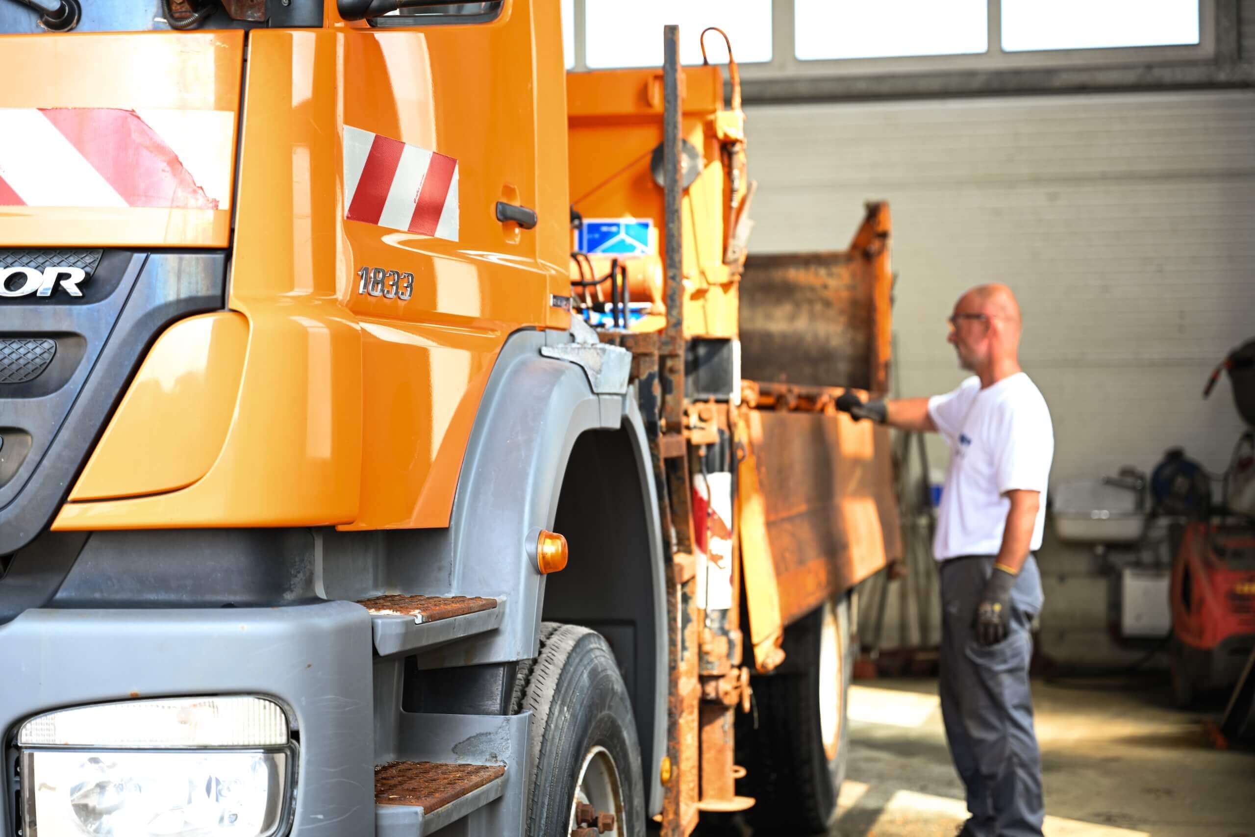 Mann arbeitet mit großem gelbem Müllwagen in Halle, Fokus auf Fahrzeugseite.